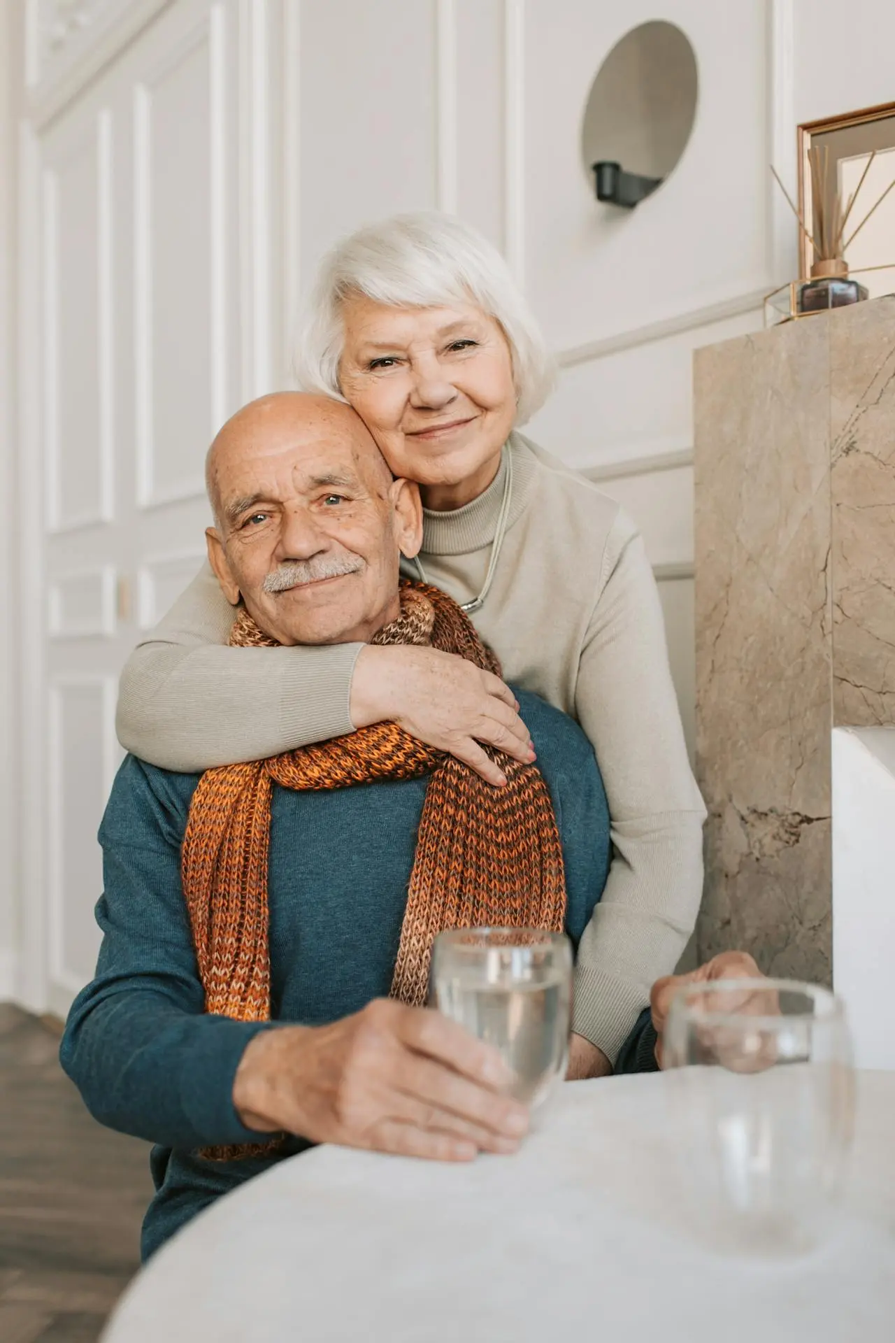 An elderly couple share a tender embrace, smiling in soft golden afternoon light