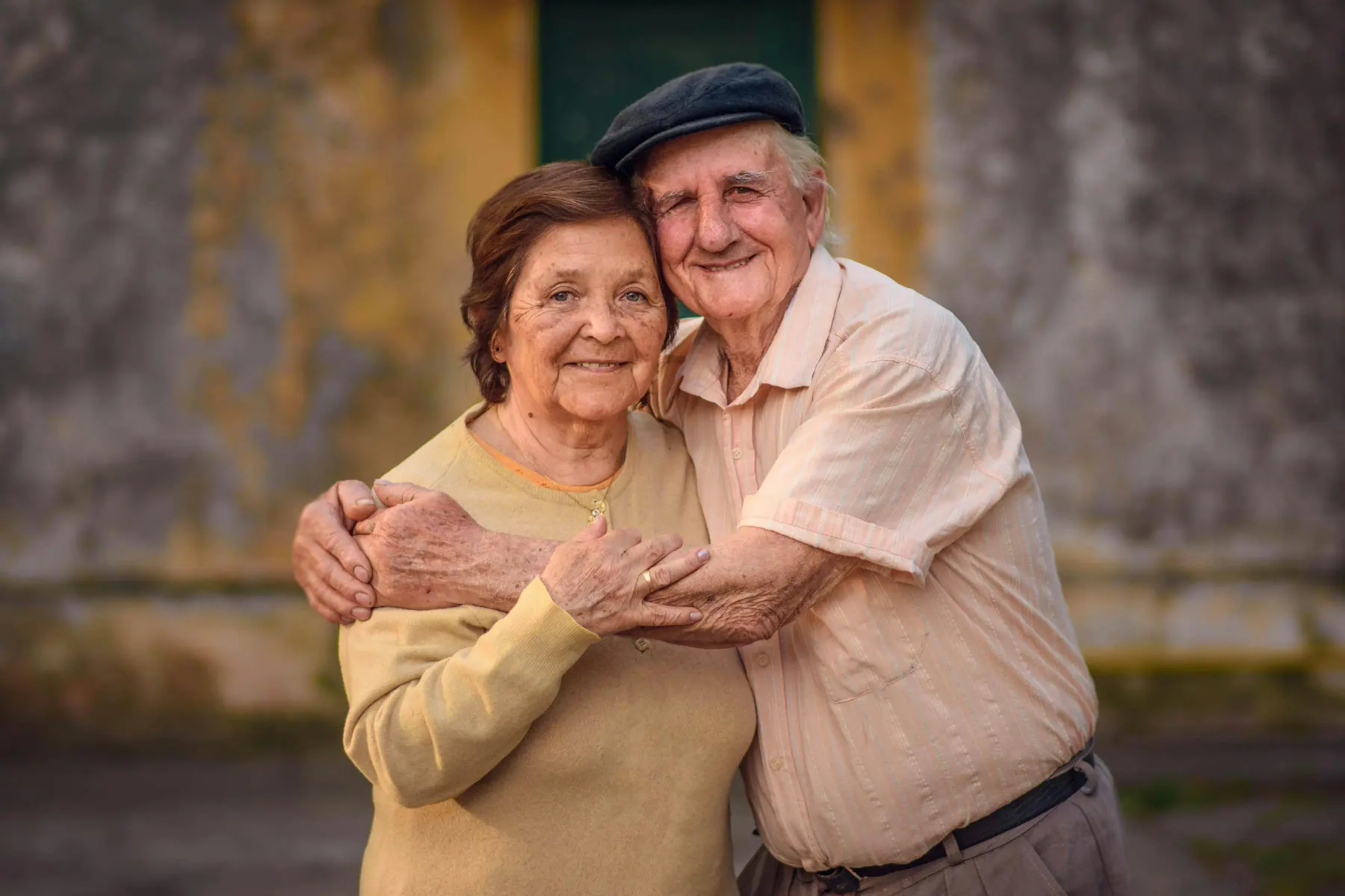 An elderly couple holds each other close in warm afternoon light, sharing a tender moment