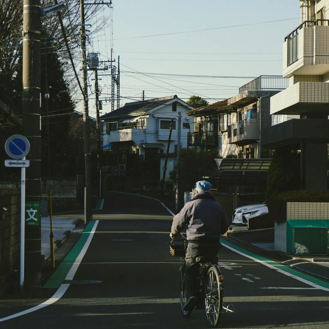 A senior rides a bicycle through a quiet residential neighborhood at golden hour